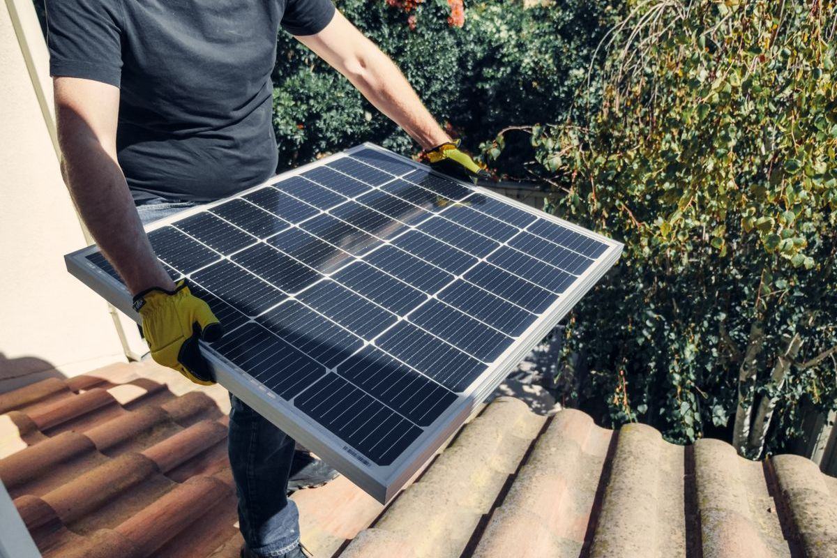 Installer lifting a solar panel onto a tiled roof
