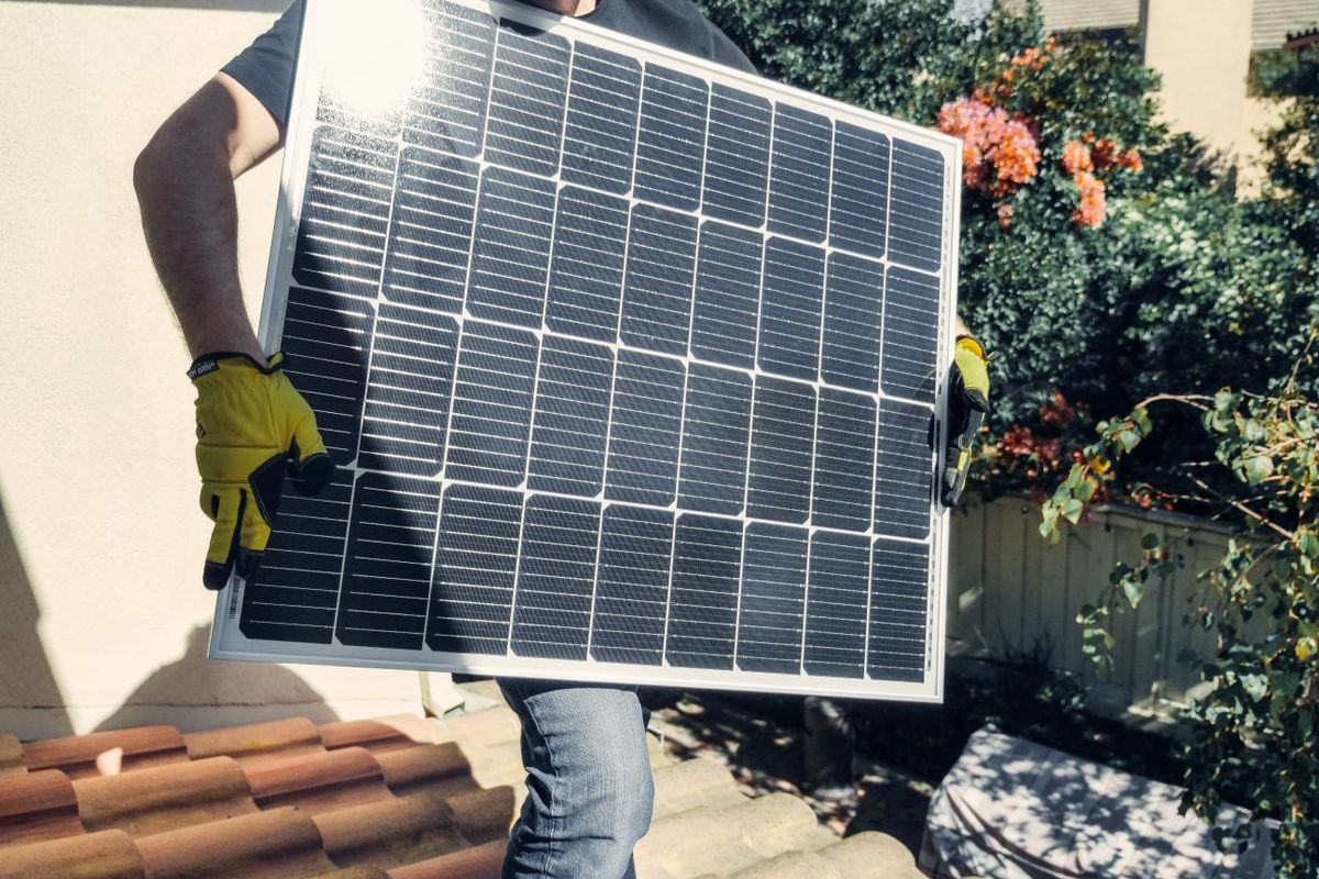 Installer carrying a solar panel across a tiled roof